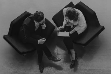 A man and woman sitting in chairs looking at a tablet representing Innovative partnerships: secure an IP prenup to ensure a happy IP marriage